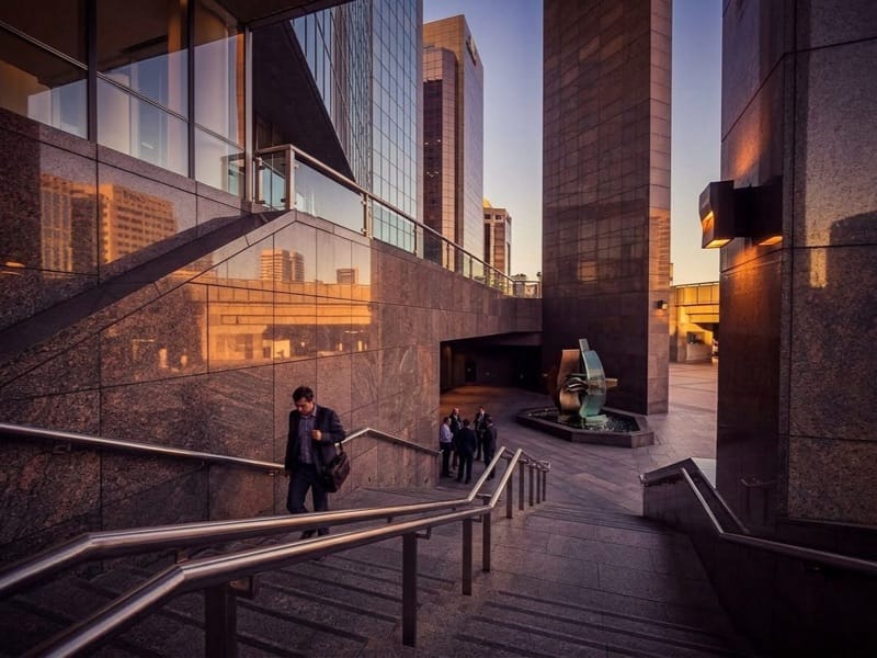 Person descending an outdoor staircase between granite office towers at sunset