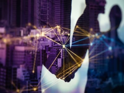 Silhouetted handshake overlaid on city high-rises and a glowing gold network of lines