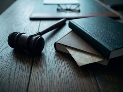 Wooden gavel beside stacked books and reading glasses on a dark wooden table