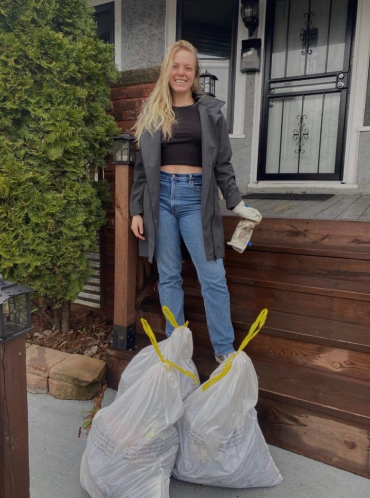 Emma Larson standing on her front porch steps with two bags of yard waste, wearing work gloves